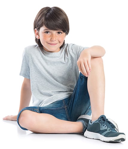 young boy with dark hair smiling sitting on the ground with one left knee raised