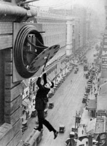 man hanging from clock on tall building
