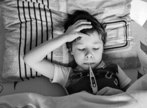 Child with thermometer in their mouth, their hand on their head